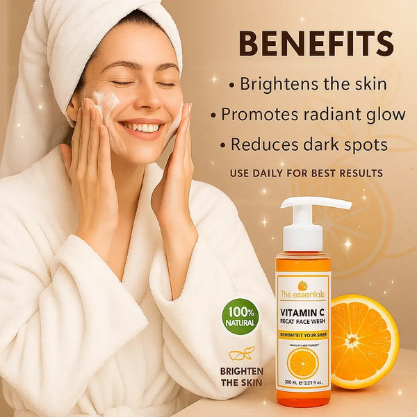 A woman in a white robe applying The Essentials Vitamin C Face Wash with a smile, next to a bottle of the bright orange gel cleanser and an orange slice. Text highlights product benefits: brightens skin, promotes glow, reduces dark spots – with "100% natural" and "brighten the skin" icons on a radiant beige background.
