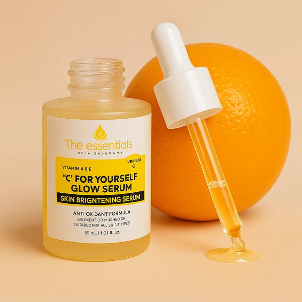 Vitamin C glow serum bottle labeled 'C For Yourself Glow Serum' by The Essentials placed beside an orange and a dropper with serum on a beige background, promoting skin brightening and antioxidant benefits.